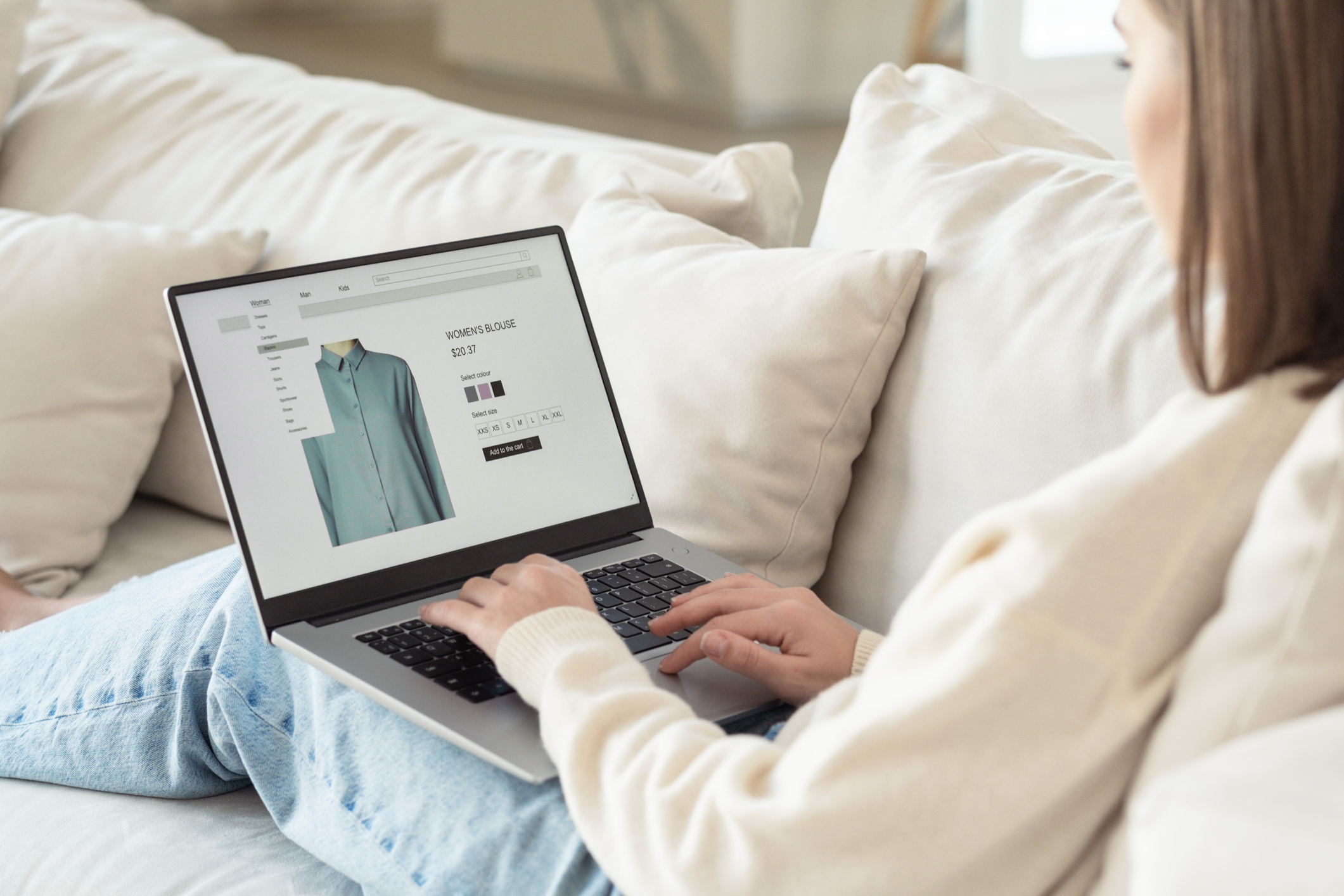 Femme assise dans un canapé consultant sur son ordinateur portable la fiche produit d’un chemisier sur une boutique en ligne. Photo de banque d’images, non générée par IA.